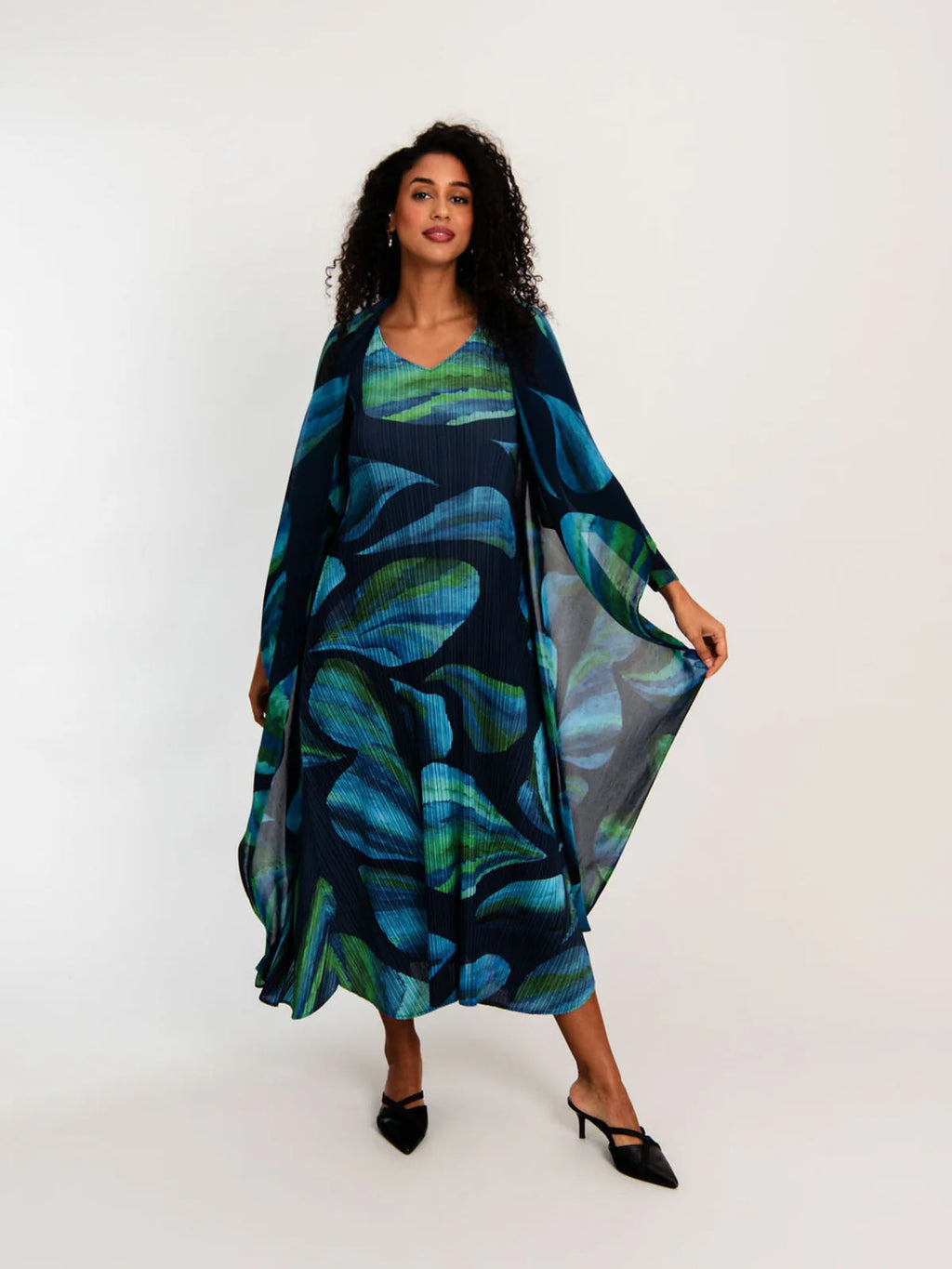 Model wearing Alquema Estrella Dress with vibrant blue and green leaf print, layered with wrap coat, stylish spring 2026 look