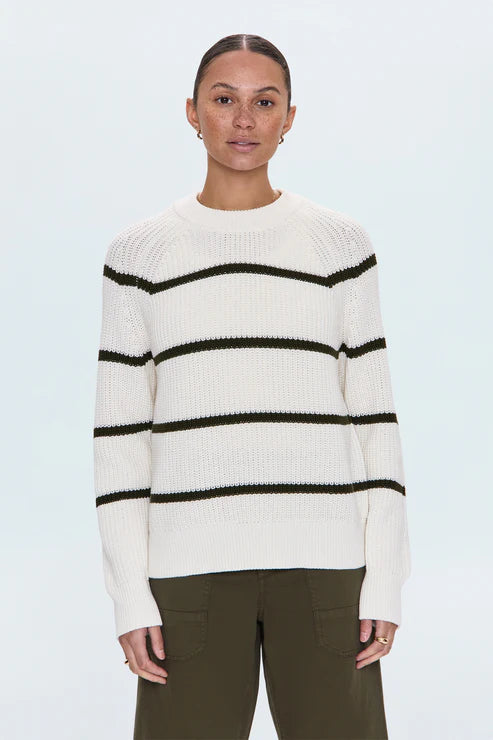 Woman in white striped knit sweater with black lines, standing with one hand in pocket