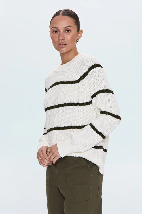 Model wearing white striped knit sweater with black lines, standing in front of a light background