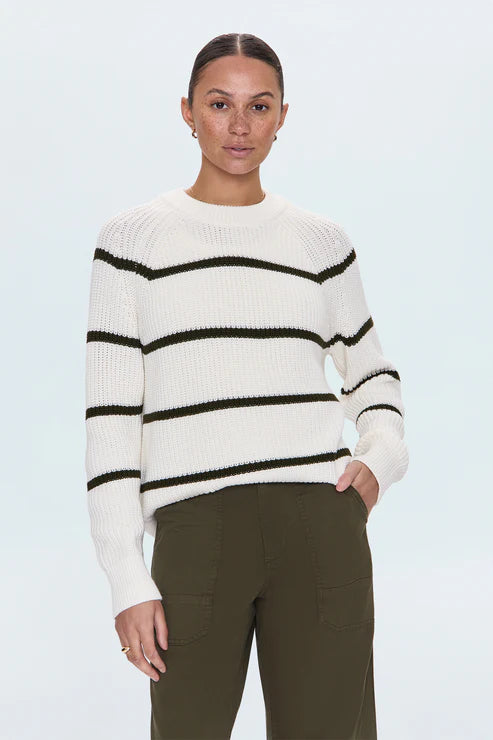 Full-body shot of woman in white striped sweater and olive green pants, posing with hands in pockets