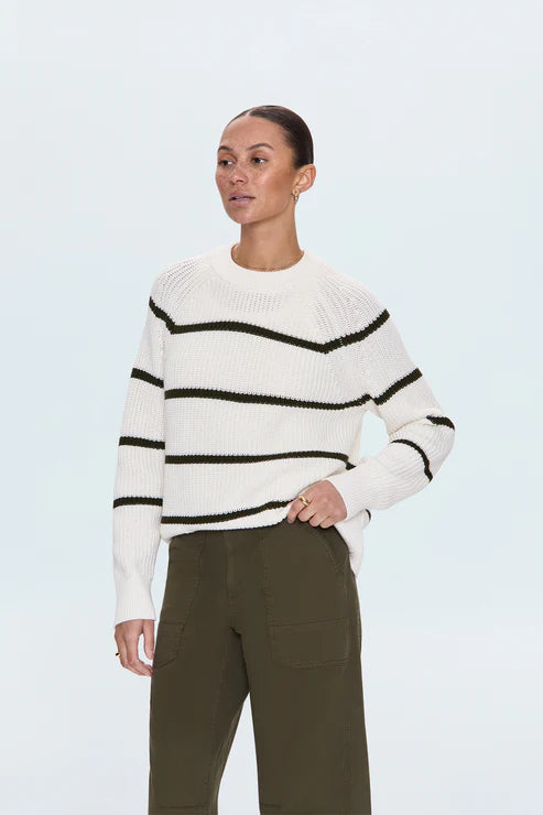Model wearing white striped sweater with black lines, standing with hand on hip